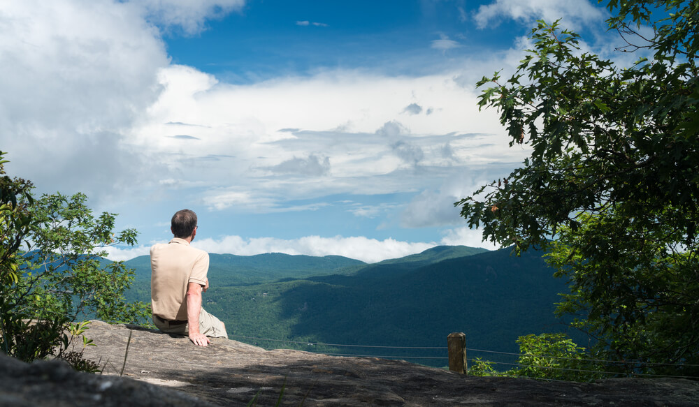 View of a person enjoying the view of mountains from the Highlands NC hiking trails